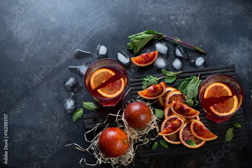 Sicilian blood oranges and their fresh juice over dark scratched metal background, high angle view with space, horizontal shot