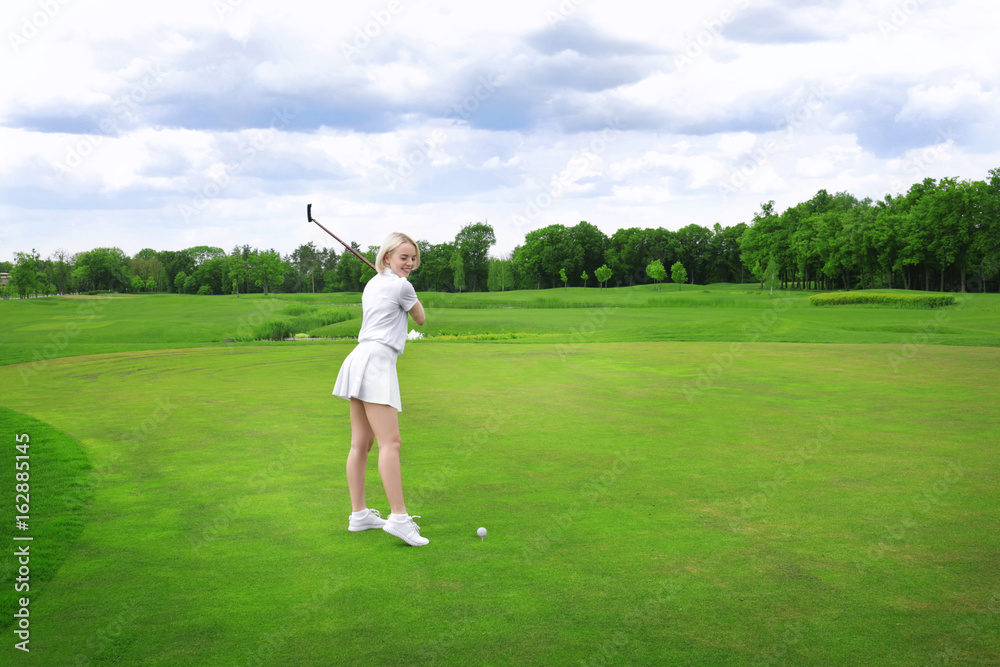 Beautiful young woman playing golf on course in summer day