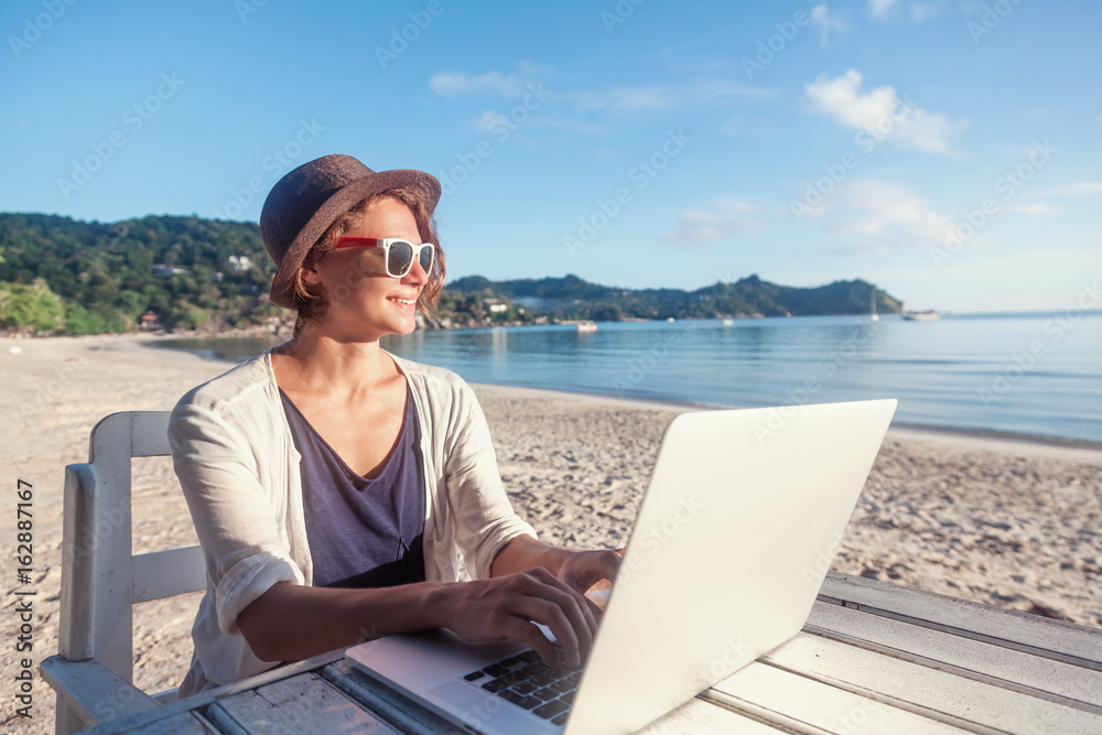 Young beautiful woman hipster traveler freelancer with laptop on the seashore. Business and vacation concept