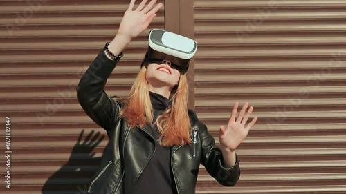 A stylish girl in virtual glasses near horizontal brown curtains. photo