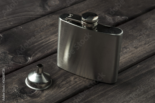 Metall hip flask with cup on wooden backdrop