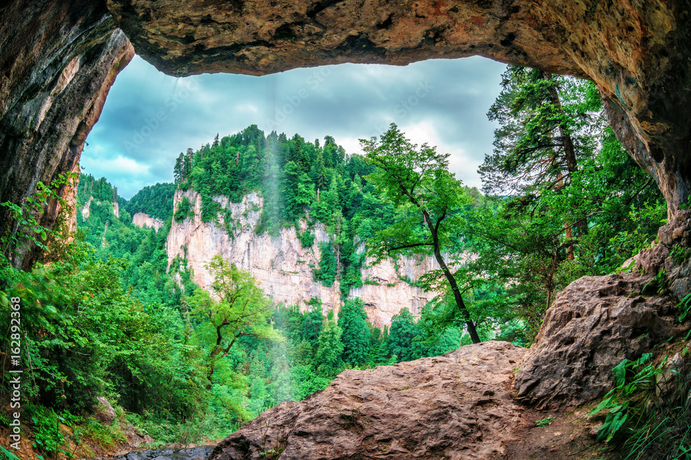 Beautiful scenic summer landscape of a rock in Kurdzhips gorge viewed from inside a weird rocky grotto with waterfall in Caucasus mountains, Russia