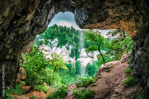 Beautiful scenic summer landscape of a rock in Kurdzhips gorge viewed from inside a weird rocky grotto with waterfall in Caucasus mountains  Russia