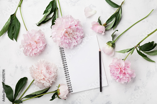Fototapeta Naklejka Na Ścianę i Meble -  Empty notebook for wedding planning, pencil and pink peony flowers on white stone table top view in flat lay style. Woman working desk.