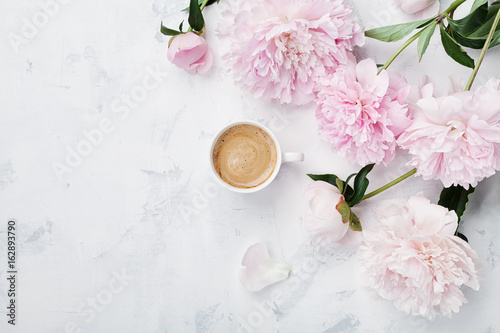 Morning coffee and beautiful pink peony flowers on white stone table top view in flat lay style. Cozy breakfast on Mother or Woman day.