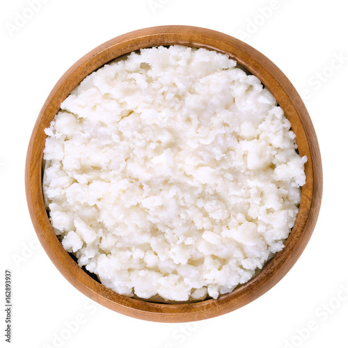Coconut puree in wooden bowl. Grated flesh and meat of coconut kernels. White, edible and raw food paste and cream. Isolated macro food photo close up from above on white background.