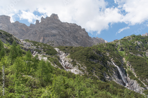 Waterfall at the foot of the dolomitic peaks and mountain hut, Dolomites, Italy