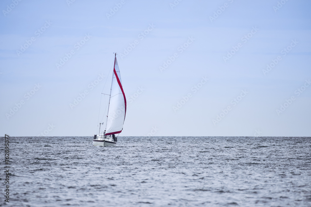 Naklejka premium Calm relaxing image of sailing boat in soft blue sky with red sail detail