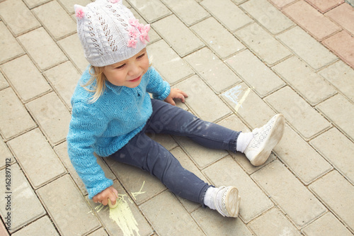 little girl draws chalk on asphalt