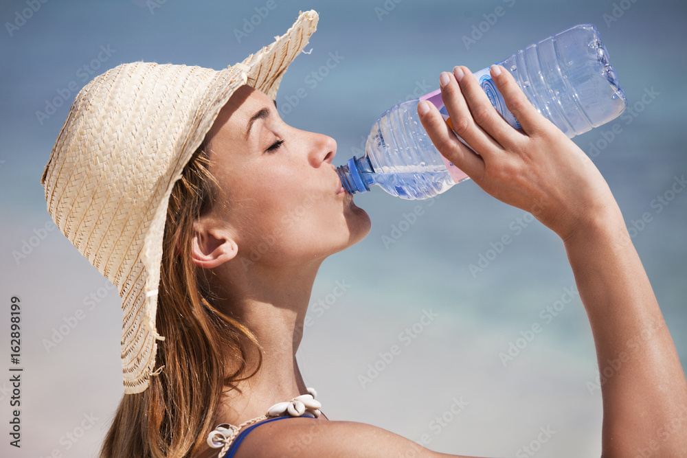 femme à la plage qui boit de l'eau avec une bouteille Photos | Adobe Stock