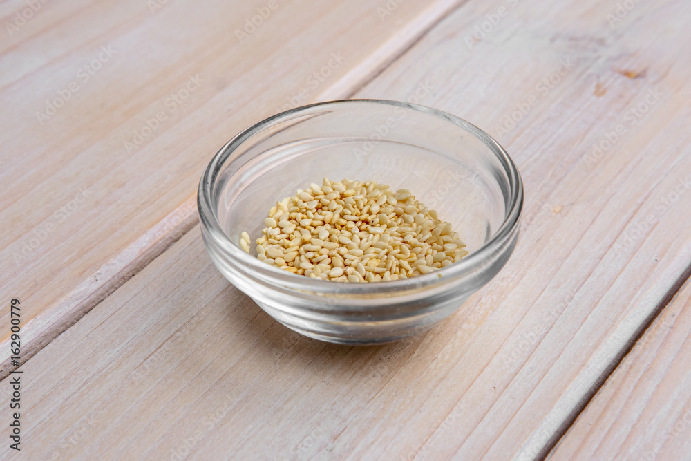 Sesame seeds in a little glass bowl on wooden table. Sesame seeds in a little glass bowl on wooden table.