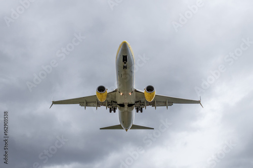 Overhead view of passenger airplane short before landing. Overcast, cloudy sky.