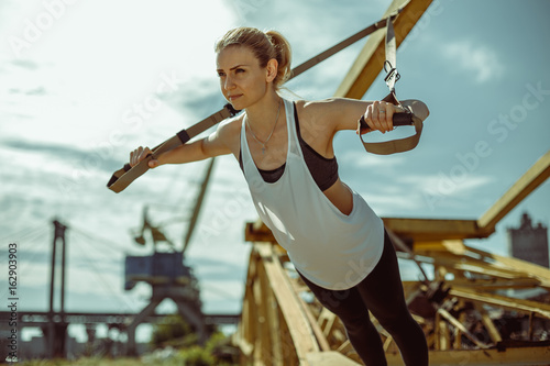 Young attractive woman does suspension training with fitness straps outdoors in the nature. © belyjmishka