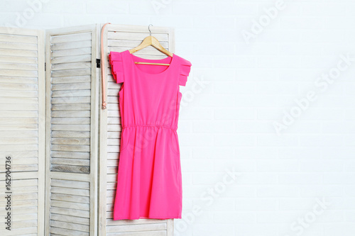 Pink dress hanging on folding screen on a grey background