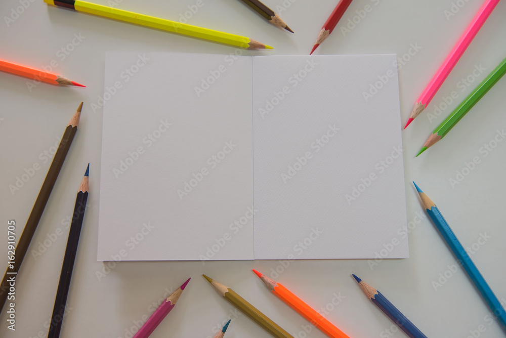 White book and colorful many crayons on the table .