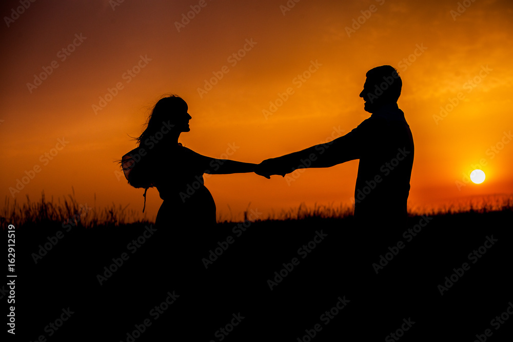 Silhouette of Happy Young Couple love Outside at Sunset. Young couple enjoying the sunset in the meadow