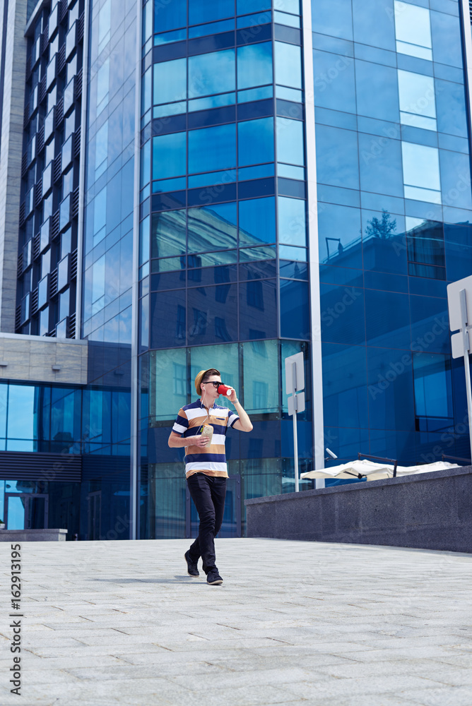 Stylish boy is walking outside and drinking coffee