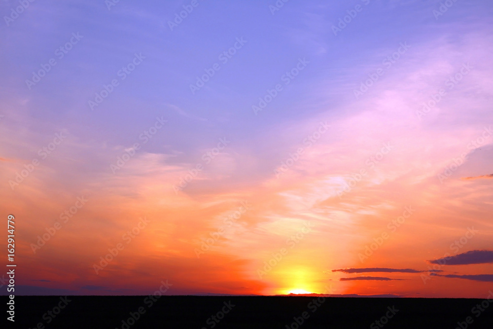 Orange sunset in summer over black earth against blue sky