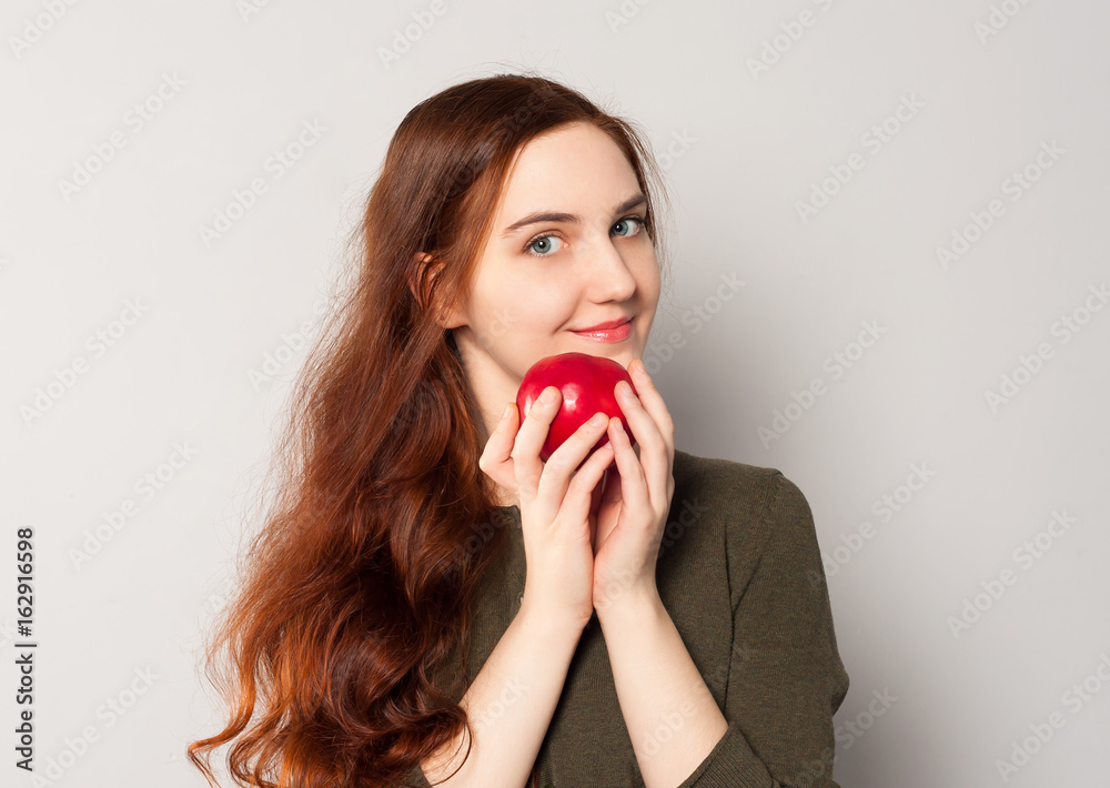 A young pretty smiling girl holding a bright red juicy ripe apple full of vitamins and fiber. Healthy vegetarian food, diet for weight loss. A young pretty smiling girl holding a bright red juicy ripe apple full of vitamins and fiber. Healthy vegetarian food, diet for weight loss.