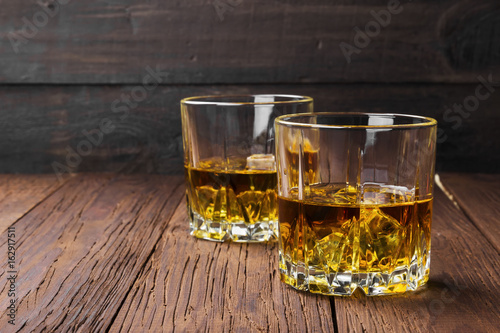 Whisky with ice in two glasses on a wooden background. Copy space. Food background