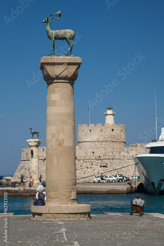 Statue Deer and hound and columns in Mandraki harbor. On background Santa Claus Fortress. Place where was statue, colossus from Rhodes. Symbolic gate to the harbor.