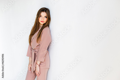 Elegant woman leaning to the white wall and staring at the camera