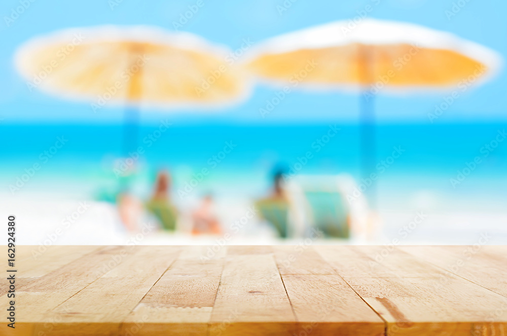 Wood table top on blur beach background with parasols, summer holiday concept