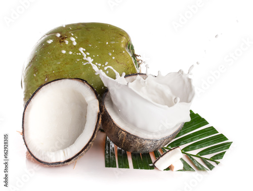 Cracked coconut with milk splash and leaf on white background.