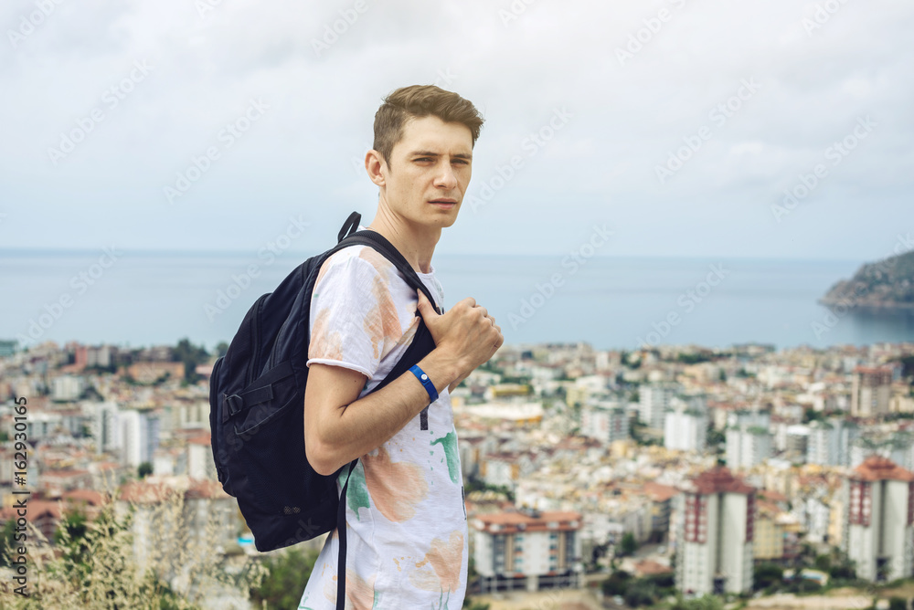 Man traveler with backpack explores the city looking at the panoramic view of the city and the coast.
