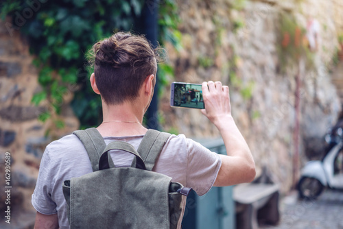 Man backpack makes a photo on your smartphone on a city street photo