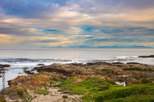 Rocky coast line on the ocean at De Kelders, South Africa, famous for whale watching. Winter season, cloudy and dramatic sky.