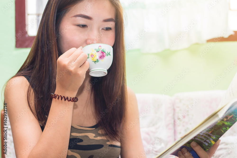 Beautiful young asian woman sitting on chair relaxing coffee time with book and smartphone at home Beautiful young asian woman sitting on chair relaxing coffee time with book and smartphone at home