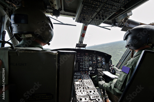 Cockpit interior details of Army helicopter with pilot and co pilot on board while flying over river. Pilot prepares to landing. photo