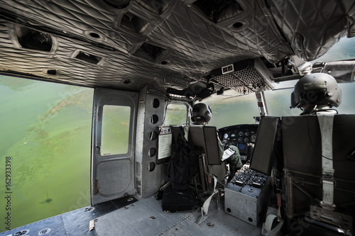 The image blurred of Cockpit interior details of Army helicopter with pilot and co pilot on board while flying over river. Pilot prepares to landing.