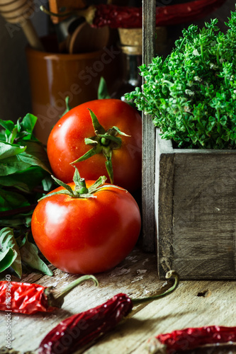 Organic ripe tomatoes with water drops  fresh thyme  green purple basil  dry chili peppers on rustic wood kitchen table  Provence mediterranean style  authentic atmosphere