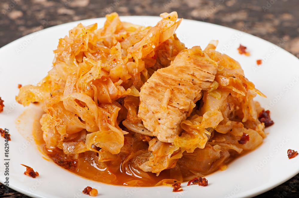 Stewed cabbage and beef meat in a white plate on an old wooden background. Stewed cabbage and beef meat in a white plate on an old wooden background.