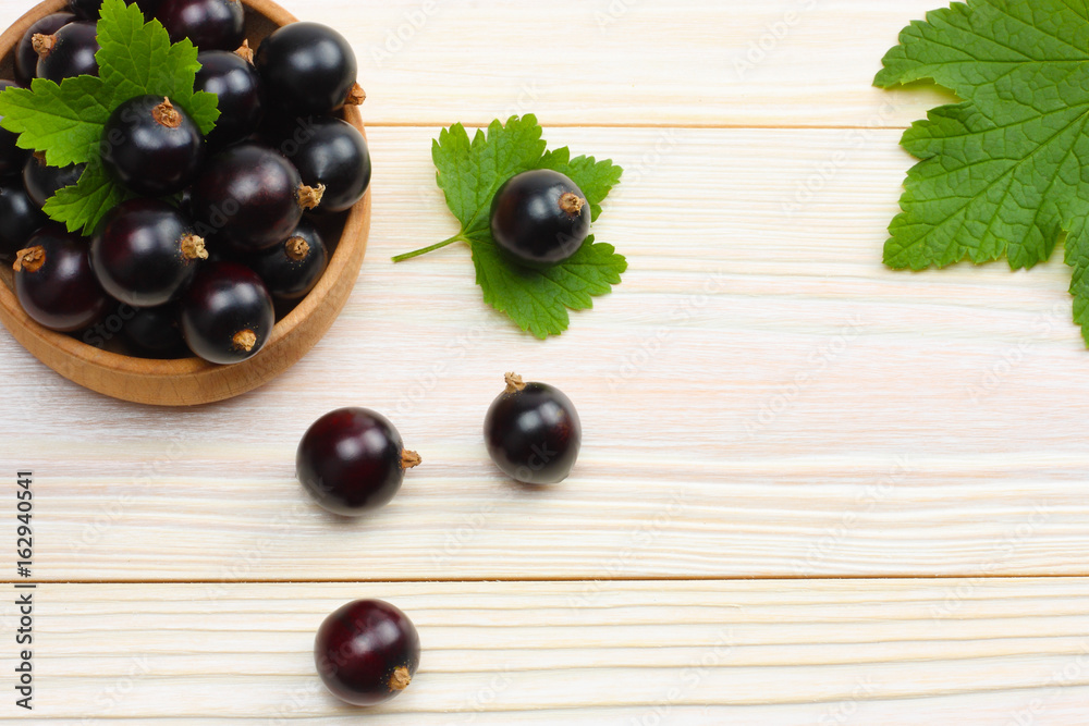 black currant in wooden bowl with green leaf on white wooden background. top view with copy space black currant in wooden bowl with green leaf on white wooden background. top view with copy space