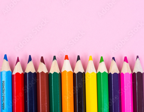Multicolored pencils on pink paper background
