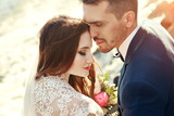 Couple hugging at sunset, lovers couple kissing in sunset. Wedding ceremony outdoors. Beautiful bride and groom with bouquet of flowers. White wedding dress for bride. Love wedding couple hug. Blurred