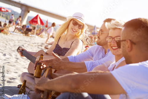 Group of friends playing guitar on the beach and having fun together