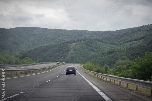 Asphalt road and car in the mountains with cloudy sky