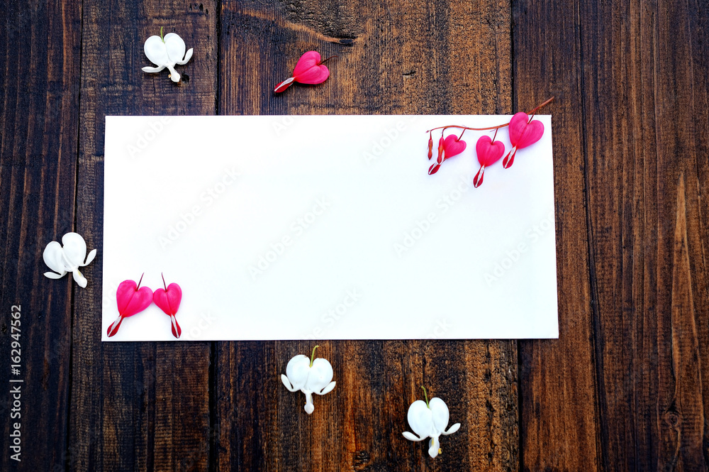 White greeting card on a wooden background with pink flowers. White greeting card on a wooden background with pink flowers.