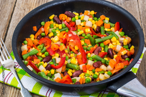 Cooked mixed vegetables in frying pan on wooden table