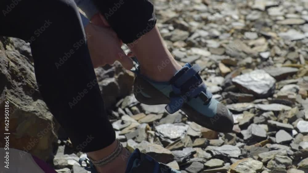 Closeup Of Young Woman Putting On Her Rock Climbing Shoes, She Secures Velcro Straps, Reaches For Her Climbing Harness Closeup Of Young Woman Putting On Her Rock Climbing Shoes, She Secures Velcro Straps, Reaches For Her Climbing Harness