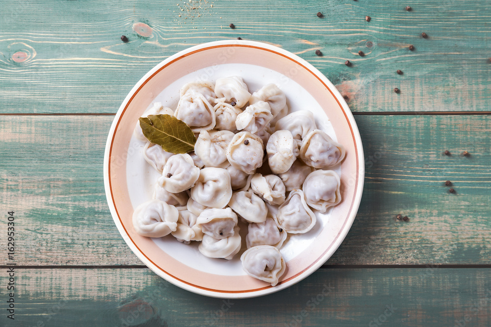 Homemade Meat Dumplings - russian pelmeni with laurel leaf on plate and green wooden background with pepper. Top view Homemade Meat Dumplings - russian pelmeni with laurel leaf on plate and green wooden background with pepper. Top view