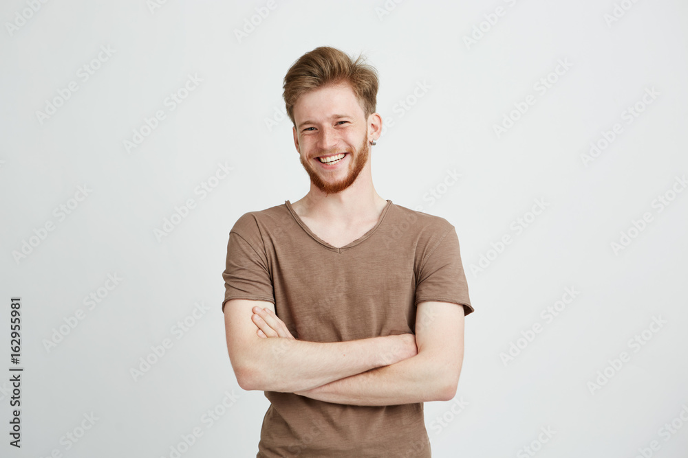 Portrait of happy cheerful young man with beard smiling looking at camera with crossed arms over white background. - obrazy, fototapety, plakaty 