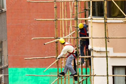 Workers working on a bamboo scaffold in Hong Kong.  People with unrecognizable faces. 