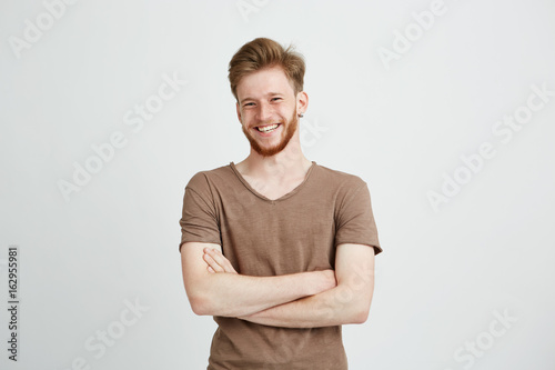 Portrait of happy cheerful young man with beard smiling looking at camera with crossed arms over white background.