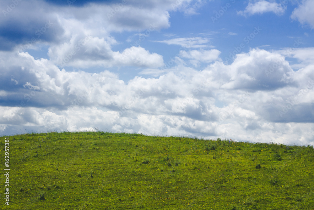 Blue cloudy sky over green grass hill landscape.