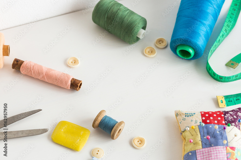 sewing tools, patchwork, tailoring and fashion concept - closeup on white desk in studio, colorful thread spools, measuring meter, buttons, many worked scissors, pincushion, equipment for needlework. sewing tools, patchwork, tailoring and fashion concept - closeup on white desk in studio, colorful thread spools, measuring meter, buttons, many worked scissors, pincushion, equipment for needlework.